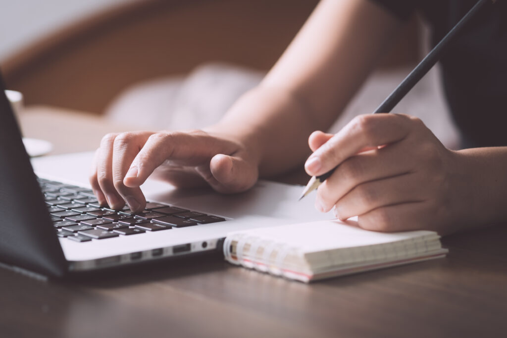 Person writing while using laptop