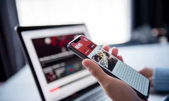 Woman reading news and articles on a smartphone and laptop, illustrating online news and digital media